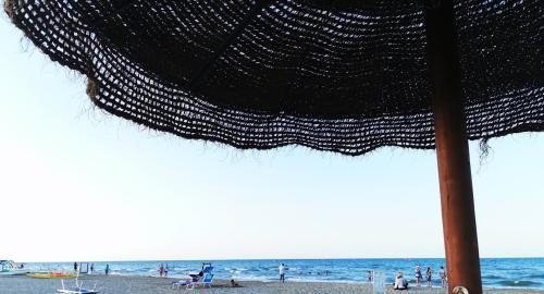 Spiaggia con ombrellone di paglia e sedie a sdraio, mare calmo.