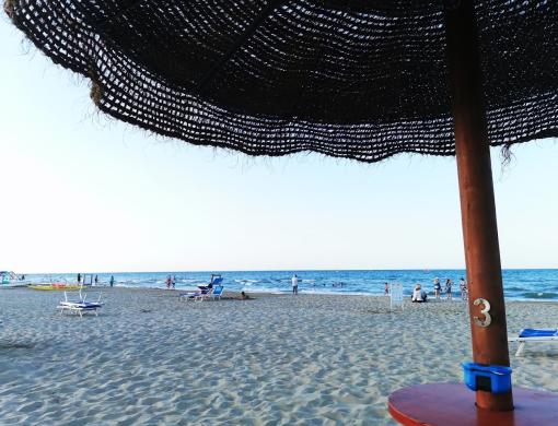 Spiaggia con ombrellone di paglia e sedie a sdraio, mare calmo.